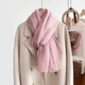 Delicate roze sjaal met elegante kantrand, hangend aan de jas, zacht en fijn detail. - Oudroze