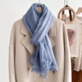 Details of the blue solid color scarf featuring delicate lace edge trim hanging on a coat. - Blue
