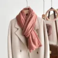 Detail view of a pink lace edge scarf draped on a beige coat, soft and elegant style. - Orange