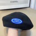 Primer plano detallado de una elegante boina de punto negra con parche de logotipo azul. - Talla única / Negro