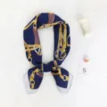 Detailopname van een donkerblauwe zijden sjaal met gouden kettingprint, elegante accessoire. - Blauwe Ketting