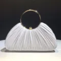 Detailed view of the white pleated satin evening clutch with a polished gold metal ring handle. - Silver
