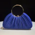 Close-up detail of the royal blue satin pleated evening clutch featuring a shiny gold ring handle. - Dark Blue