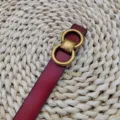Vue détaillée d'une ceinture en cuir bordeaux avec anneaux doubles dorés et boucle carrée vintage. - Rouge