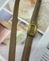 Detail view of women's thin leather belt in khaki with retro gold square buckle, stylish. - Beige