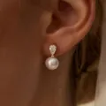 Primer plano detallado de elegantes aretes colgantes de circonita en forma de pera y perla. - Estilo 1 Dorado