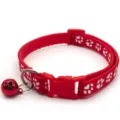 Close-up detail shot showing a red nylon pet collar featuring white paw prints and a red bell. - Red