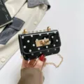 Close-up view of a stylish black patent leather polka dot mini shoulder bag with gold chain. - Black Polka Dot