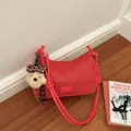 Red woven shoulder bag detail showing the front badge, knotted strap and a cute plush dog charm. - Red With Charm
