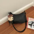 Detail shot of stylish black woven shoulder bag with cute plush pendant on wooden floor. - Black With Pendant
