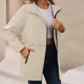 Beige hooded waterproof windbreaker jacket with black zippers and stylish waist ruffle detail. - Apricot