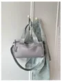 Vista detallada del bolso bandolera cilíndrico gris colgado junto a una chaqueta vaquera. - Gris