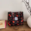 Vista detallada del bolso tote floral negro con estampado de fresa, correas de cadena y etiqueta. - Negro