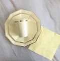 Gros plan detaille de vaisselle jetable jaune clair avec bordures dores pour fetes. - Service de 4 pièces : Grandes et petites assiettes, gobelets, serviettes / Assiettes décagonales jaune avec dorure
