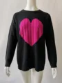 Detailaufnahme schwarzer Strickpullover mit pinkem Zopfstrick Herz Motiv und Rundhalsausschnitt. - Schwarz-Rosenrot