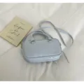 Close-up view of a light blue shoulder bag on a clean white fabric background with prop book. - Blue Without Charm