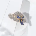 Detailed view of rhinestone hat brooch with blue bow, elegant lapel pin accessory. - Gold