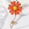 Detailopname van een oranje geëmailleerde madeliefjesbroche met een gouden stengel erbij. - Legering / Oranjerood