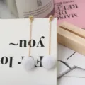 Gedetailleerd overzicht van trendy lange oorbellen met witte pompons en goudnoppen. - Grijs