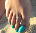 Close-up detail of a vintage spiral toe ring worn on the foot at a beach setting. - Antique Silver