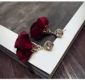 Close-up detail shot of elegant dark red fabric rose flower earrings featuring sparkly rhinestone studs. - Burgundy
