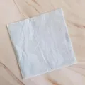 Close-up detail of a clean white paper napkin with embossed border texture on tabletop. - 16 Sheets of 33x33 Napkins in Blue