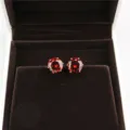 Detailed view of round 8mm red zircon stud earrings in a brown velvet jewelry box. - Gold + Red