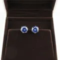 Detailed close-up shot of round blue cubic zirconia stud earrings displayed on brown velvet. - Gold + Blue