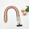 Vue de détail de la lanière de téléphone tressée avec connecteur en cuir et fermoirs dorés. - 80cm / Curcuma