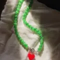 Dettaglio collana di perle occhio di gatto verde con ciondolo a cuore rosso su stoffa. - Taglia unica / Collana di Pietra Occhio di Gatto Verde con Ciondolo a Cuore Rosso (43cm) / Verde