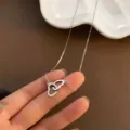 Elegante collar de acero de titanio plateado con colgante de corazón hueco entrelazado, vista manual. - Plateado
