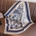 Detailansicht eines blau-weißen Seidenschals mit Landschaftsdruck auf braunem Sofa - 70x70cm / Marineblau