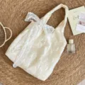 Détail de la broderie de rose et du nœud en dentelle sur un sac cabas beige - Sac de Gilet Rose Ajouré + Pendentif Fleur Blanche