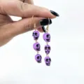 Detailed close-up of purple skull dangling earrings, gothic style, perfect for Halloween. - Purple Drop Style