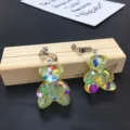 Close-up detail of cute handmade resin glitter bear clip-on earrings with sparkly colorful flakes. - Clip-On Earrings / Yellow