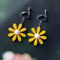 Primer plano de pendientes de clip de margarita amarilla con centro blanco y cierres plateados. - Estilo de Clip de Oreja Espiral / Amarillo