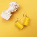 Nahaufnahme Detailaufnahme kreativer gelber Miniatur-Ölfass-Ohrringe mit Kunstskulptur-Requisite. - Haken-Stil / Gelb