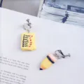 Detailed view of creative handmade student asymmetrical earrings featuring funny pencil and paper design. - Clip-on Earrings / Yellow