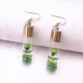 Detailed shot of handmade glass bottle earrings featuring green preserved flower and glitter. - Green