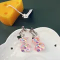 Primo piano dettagliato di orecchini clip con orsetto in resina iridescente su piatto. - Orecchini a clip / Rosa