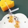 Primo piano di orecchini ad orsetto iridescenti con clip su vassoio bianco con candela - Orecchini a clip / Oro