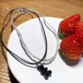 Nahaufnahme der doppelreihigen Perlenkette mit schwarzem Bärenanhänger und Erdbeeren. - Schwarz