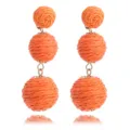 Detailopname van handgemaakte oranje raffia rotan bal lange bungelende oorbellen voor strand. - Oranje