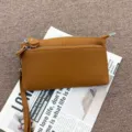 Detailed view of the brown genuine leather multi-zipper clutch bag with practical wrist strap. - Caramel color