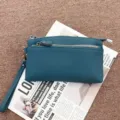 Close-up detail of genuine leather clutch bag with zipper pocket and wrist strap design. - Teal