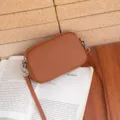 Vista detallada del bolso cruzado marrón de cuero genuino, con un diseño compacto y elegante. - Caramelo