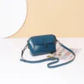 Primer plano detallado del bolso cruzado azul de cuero encerado con textura fina y herrajes. - Verde azulado