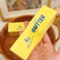 Detailed view of a yellow realistic butter stick squishy decompression toy held in hand - 喷漆高品质款 / About 14cm