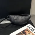 Detail view of black leather croissant shoulder bag showing pleat texture and metal zipper. - Black