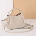 Vista detallada de un elegante bolso tipo cubo de cuero beige con asas y correa cruzada. - Marfil